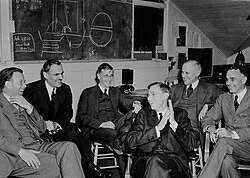 Scientists gathered in front of a chalkboard diagram